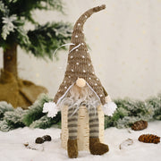 Knitted gnome ornament with polka dot hat and striped legs sitting on birch log.