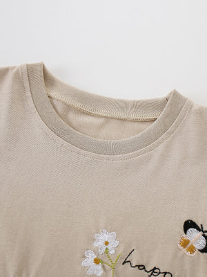 Beige cotton tee with embroidered daisies, butterfly, and "happ" text detail.