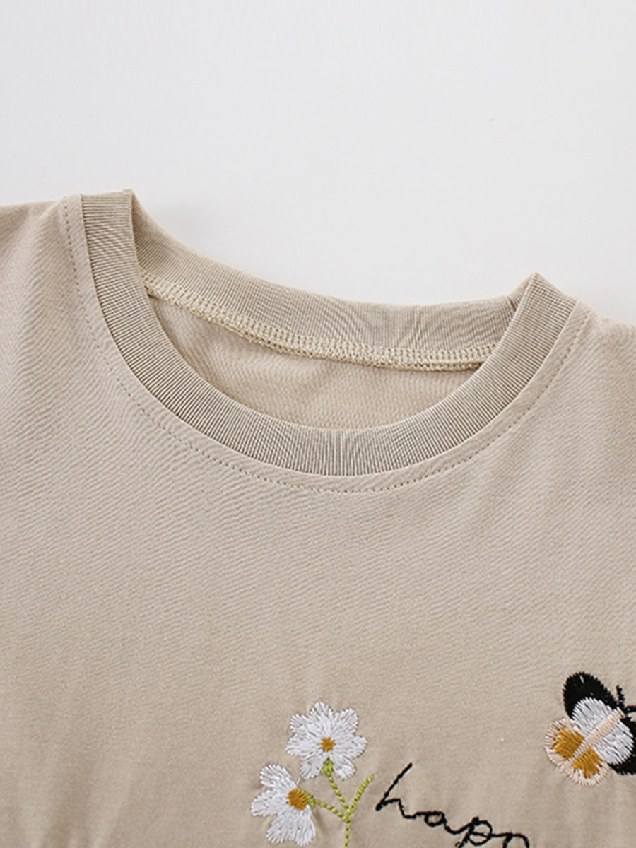 Beige cotton tee with embroidered daisies, butterfly, and "happ" text detail.
