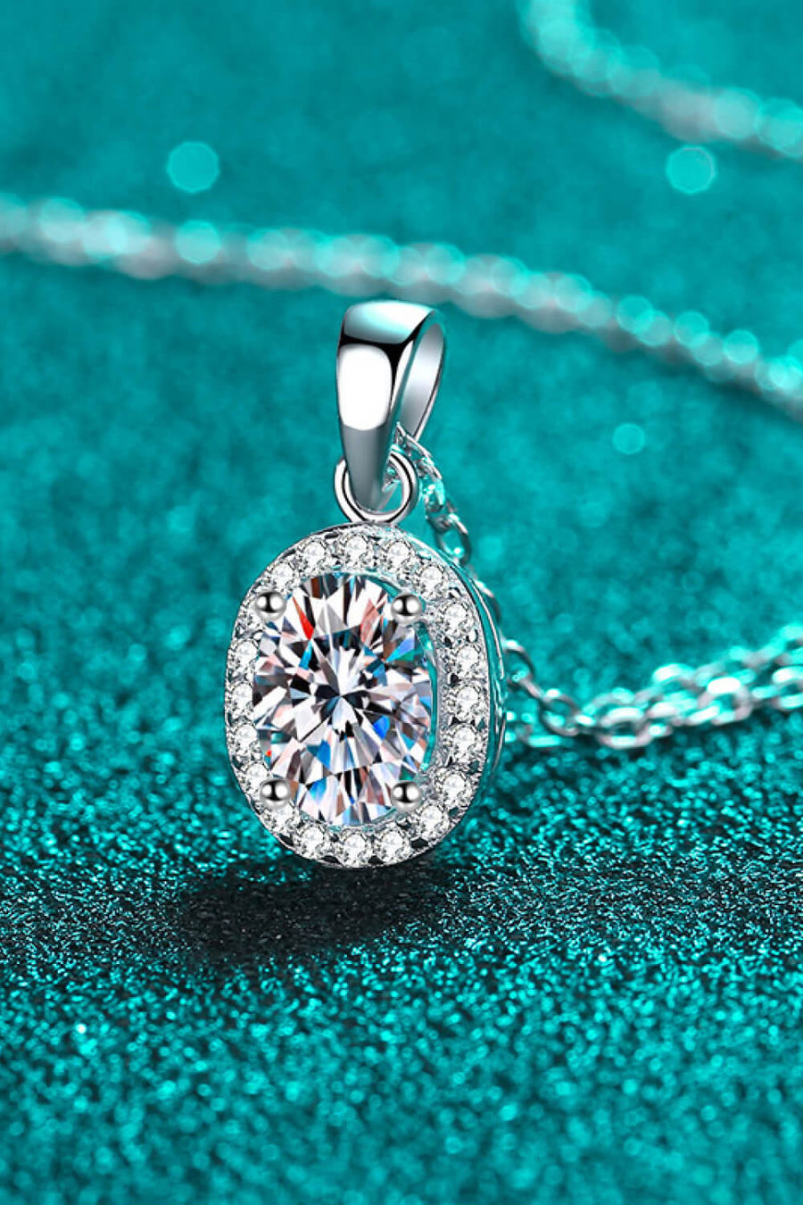 Silver halo moissanite pendant necklace with oval cut center stone and diamond accent halo on sterling silver chain.