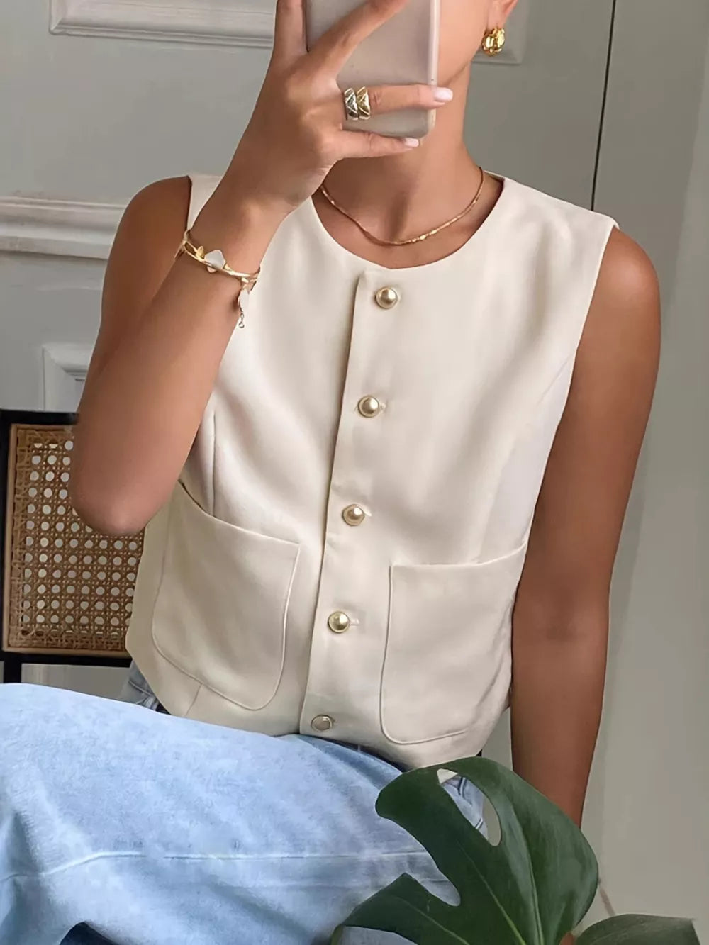 Cream button-down sleeveless vest with crew neck, gold buttons, and pocket details.
