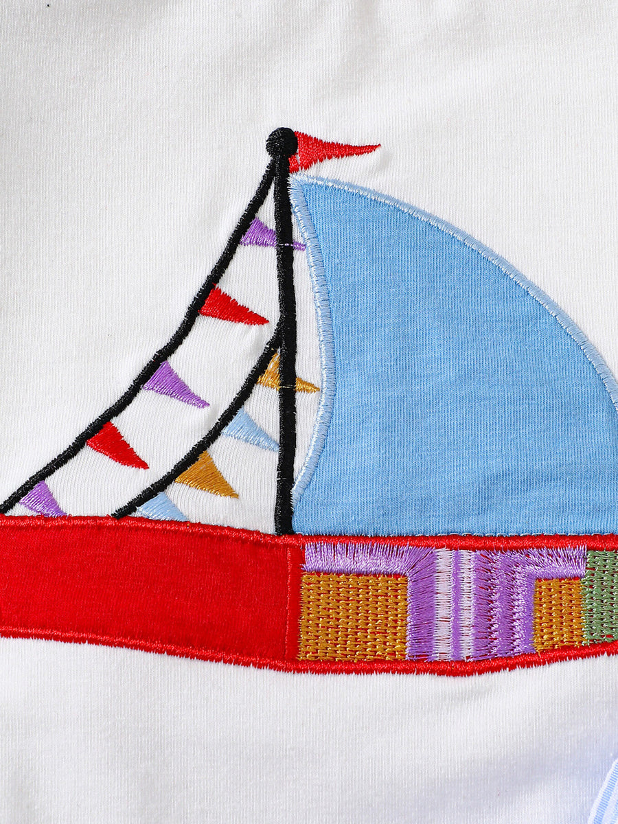 White baby tee with sailboat appliqué and colorful flags.