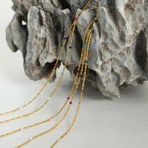Gold necklaces with colorful beads and gold bar accents cascade down, featuring red, black, white, orange, and turquoise