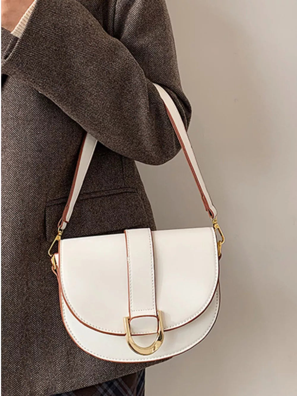 Chic white semi-circular flap crossbody bag with gold hardware and brown trim.