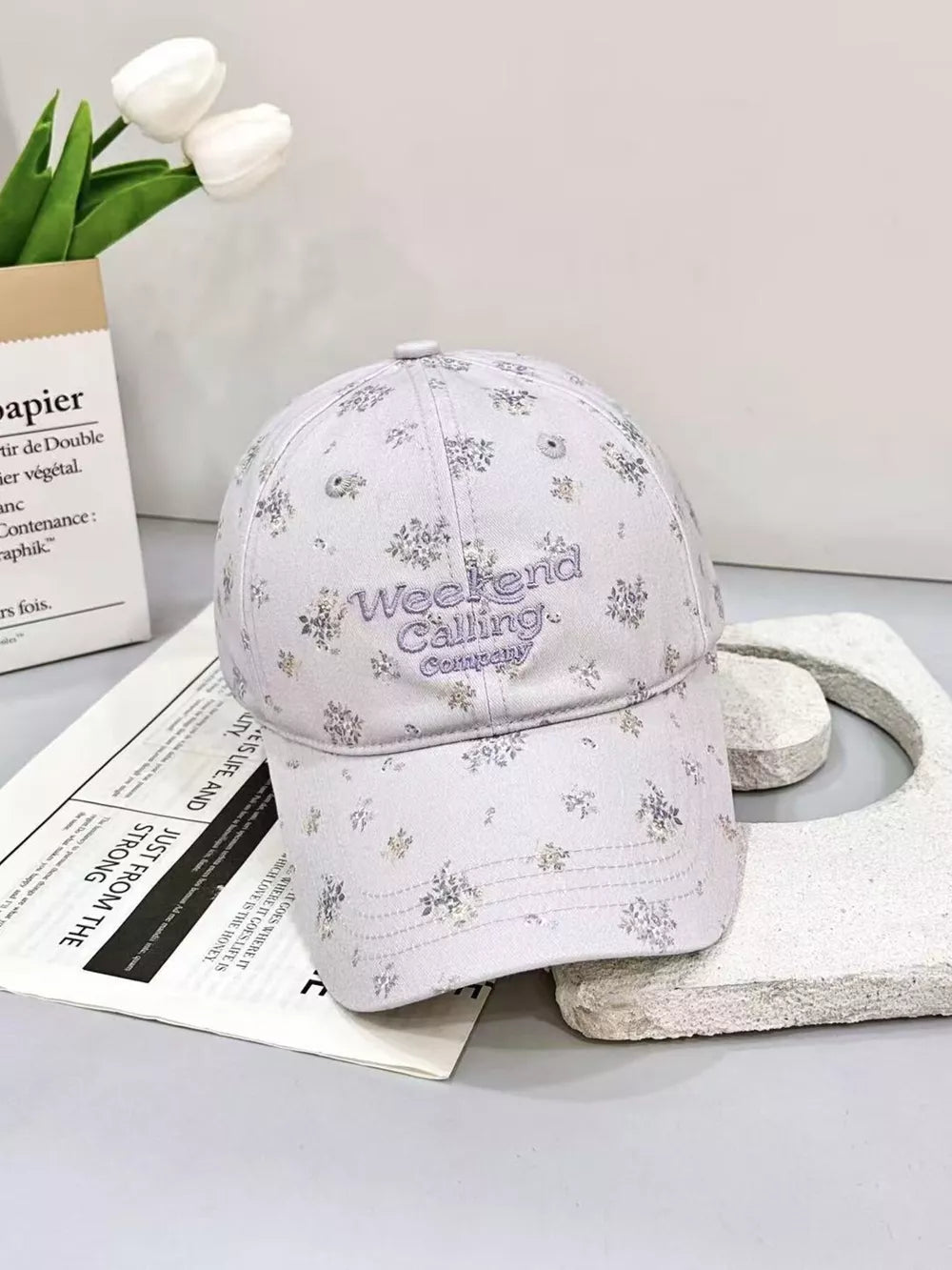 Embroidered floral baseball cap in light purple with "Weekend Calling Company" text detail.