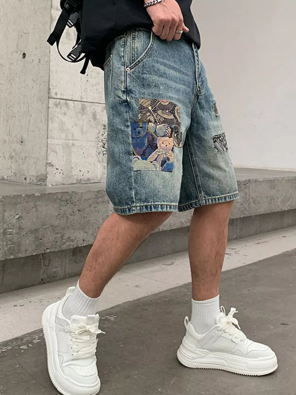 Men's blue denim shorts with graphic patchwork details and a relaxed fit.