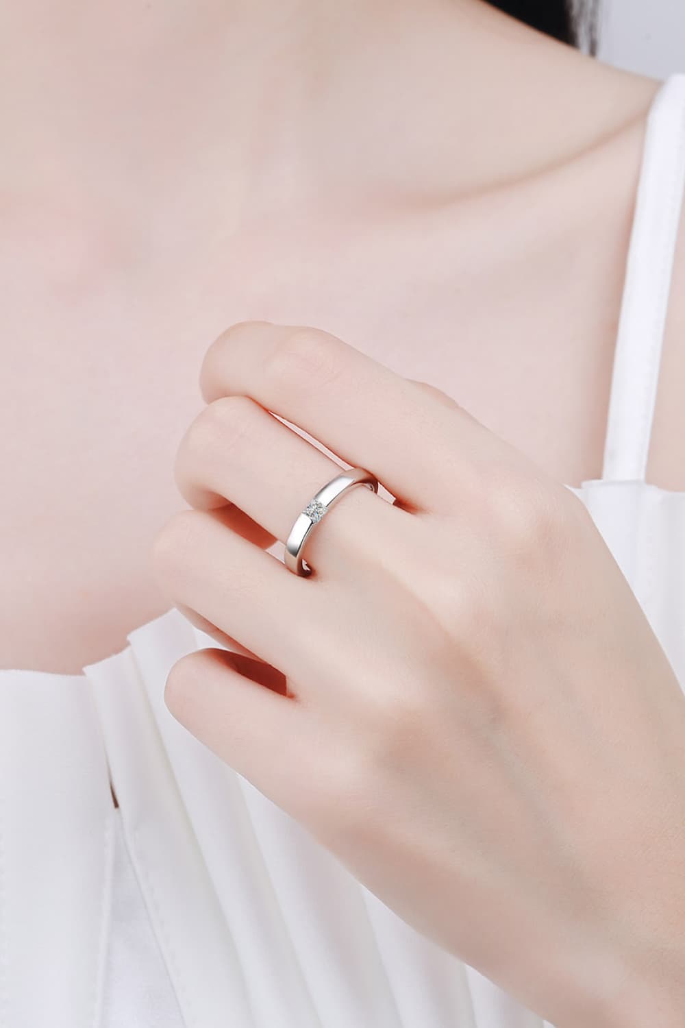 Silver band ring with a single clear solitaire stone, on a hand.
