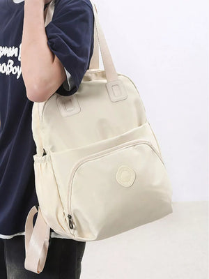 Off-white Oxford cloth backpack with adjustable straps and zippered pockets.