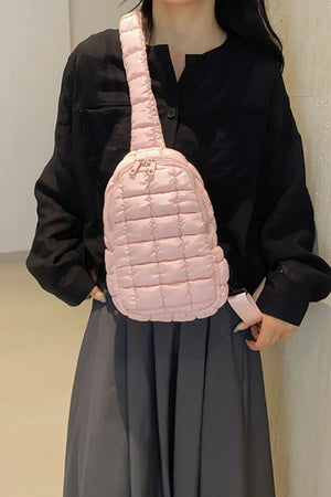 Padded sling bag in blush pink with quilted texture and top handle.