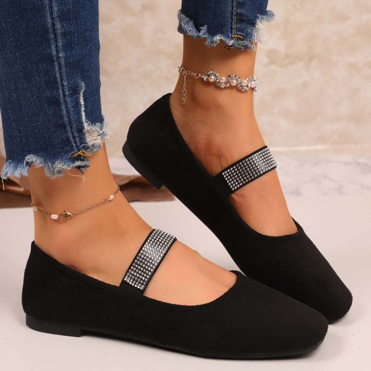 Black slip-on flats with square toe and rhinestone strap detail.