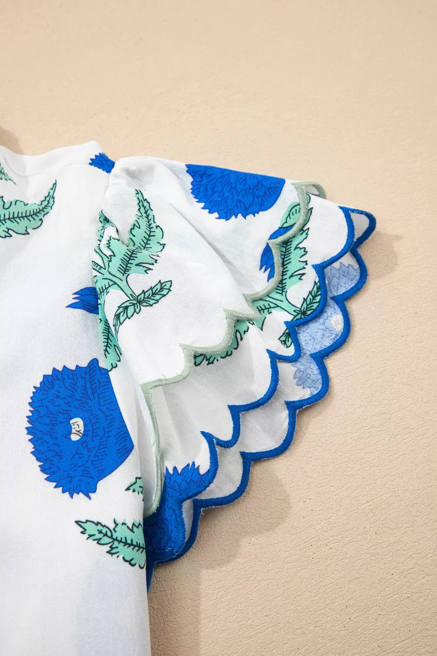 White cotton blouse with blue floral print and scalloped sleeves.