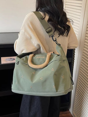 Duffel bag in sage green canvas with embroidered bows and tan handles.