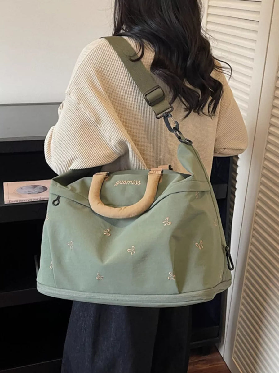 Duffel bag in sage green canvas with embroidered bows and tan handles.