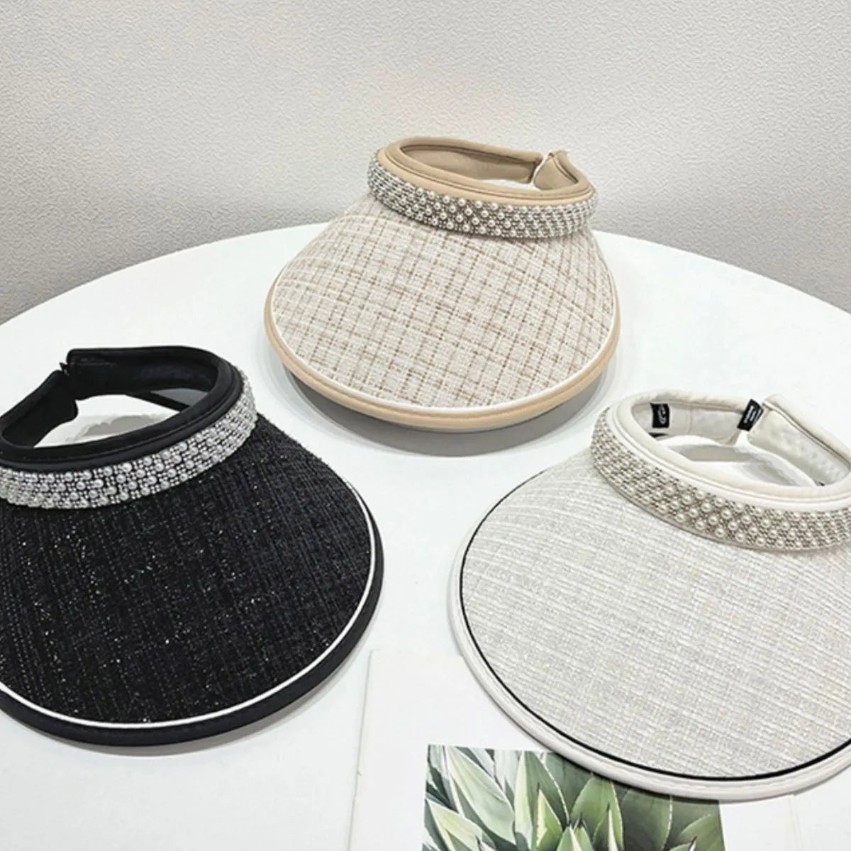 Pearl embellished tweed visors in beige, black, and white with wide brims.