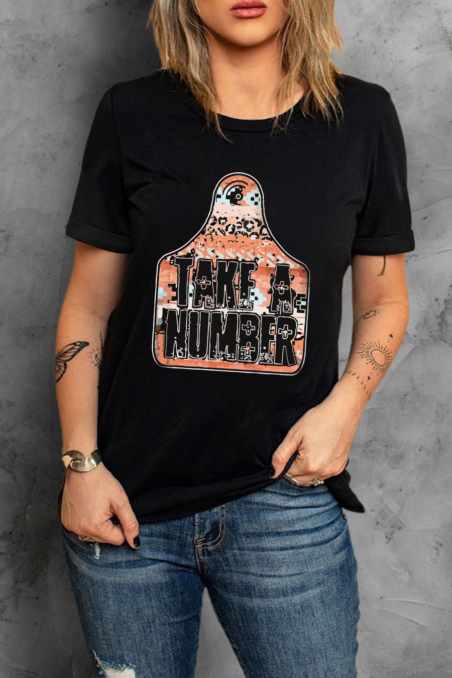 Black graphic t-shirt with "Take A Number" text on a cow tag shaped graphic with leopard print and pixelated pattern.