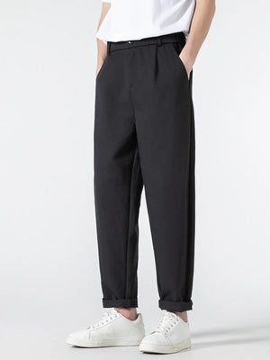 Black casual pleated trousers with a loose fit and cuffed hems, styled with white sneakers.