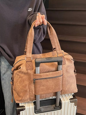 Brown canvas duffel bag with luggage sleeve and zippered pocket, styled with a grey sweatshirt.