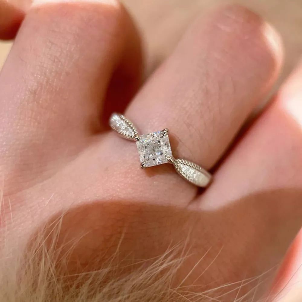 Sterling silver ring with princess-cut moissanite and geometric band.