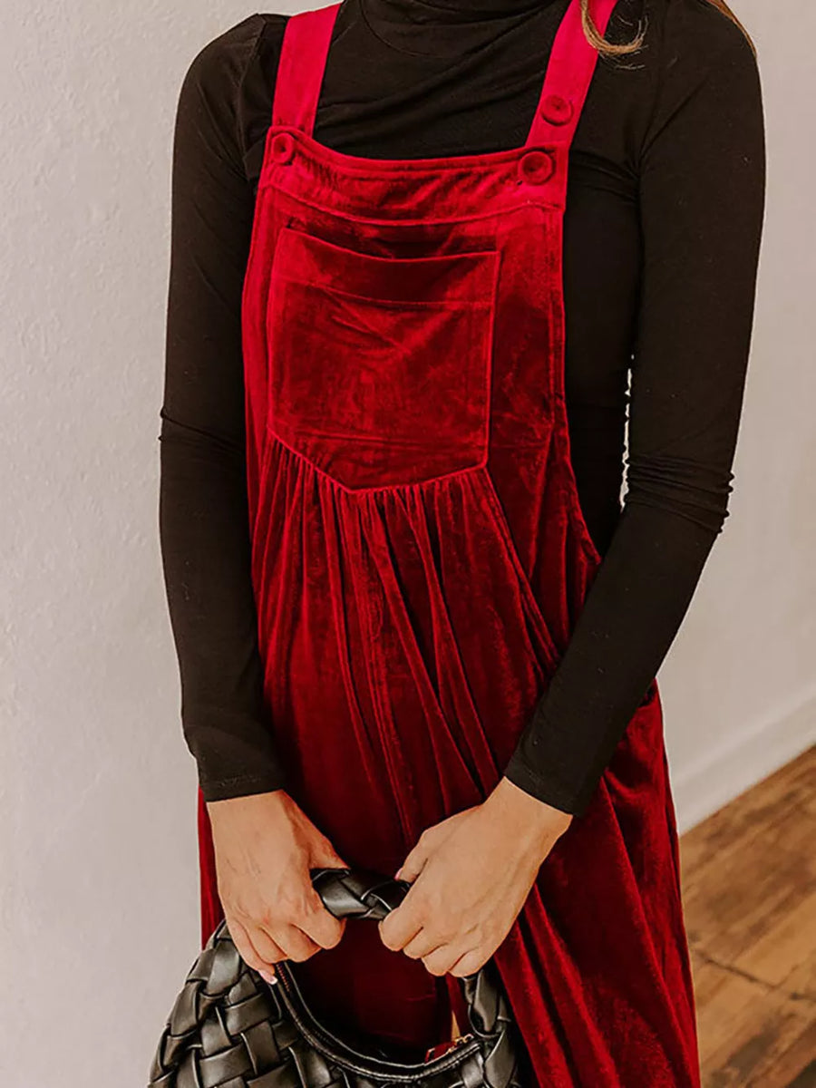 Burgundy velvet romper with wide legs, bib pocket, and button straps over a black turtleneck.