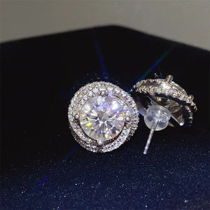 Halo diamond cluster stud earrings in silver with a central round-cut stone surrounded by smaller stones.