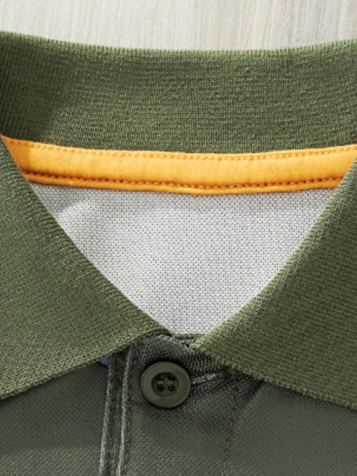 Children's green polo shirt with orange trim and a dark button.