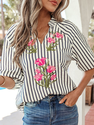 Striped V-neck blouse with bright pink floral embroidery and short sleeves.