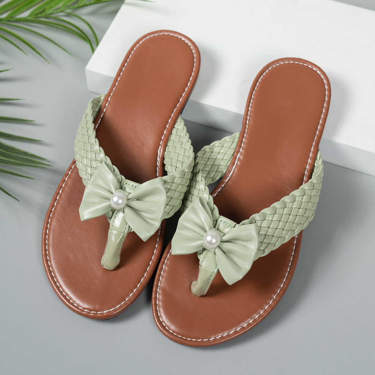 Green bow embellished flat thong sandals with woven straps and pearl detail.
