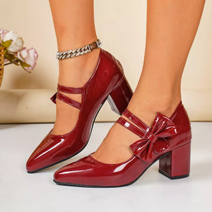 Red patent leather block heel pumps with pointed toe and bow detail.