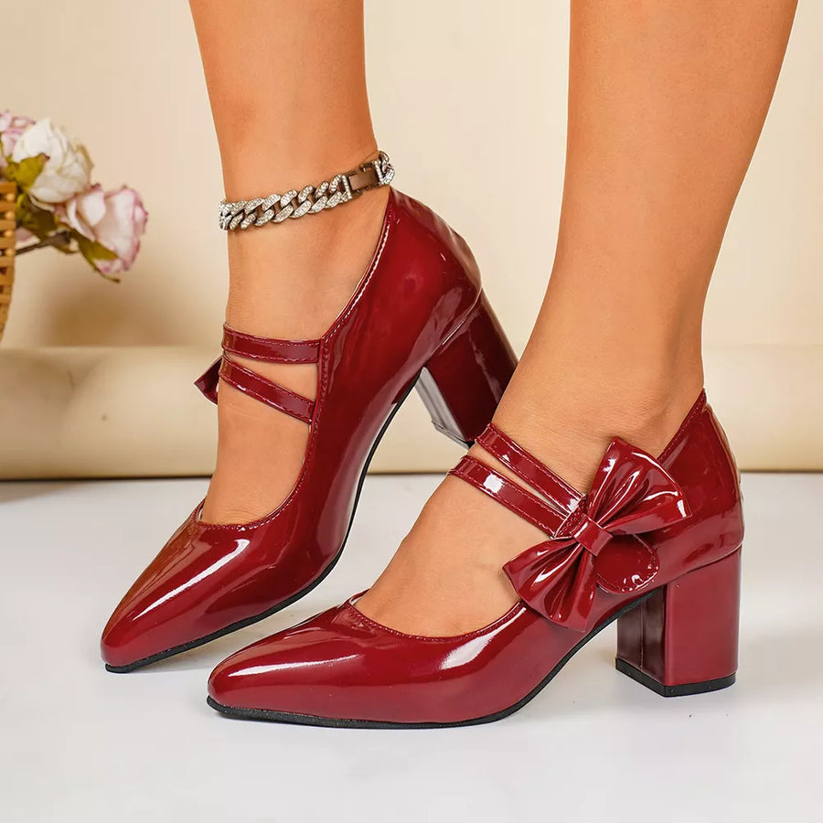 Red patent leather block heel pumps with pointed toe and bow detail.