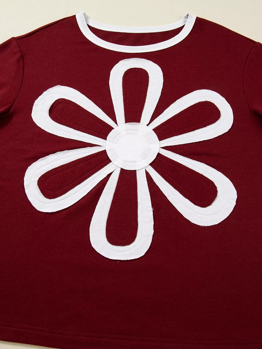 Burgundy long-sleeve top with white flower patch detail and white trim neckline.