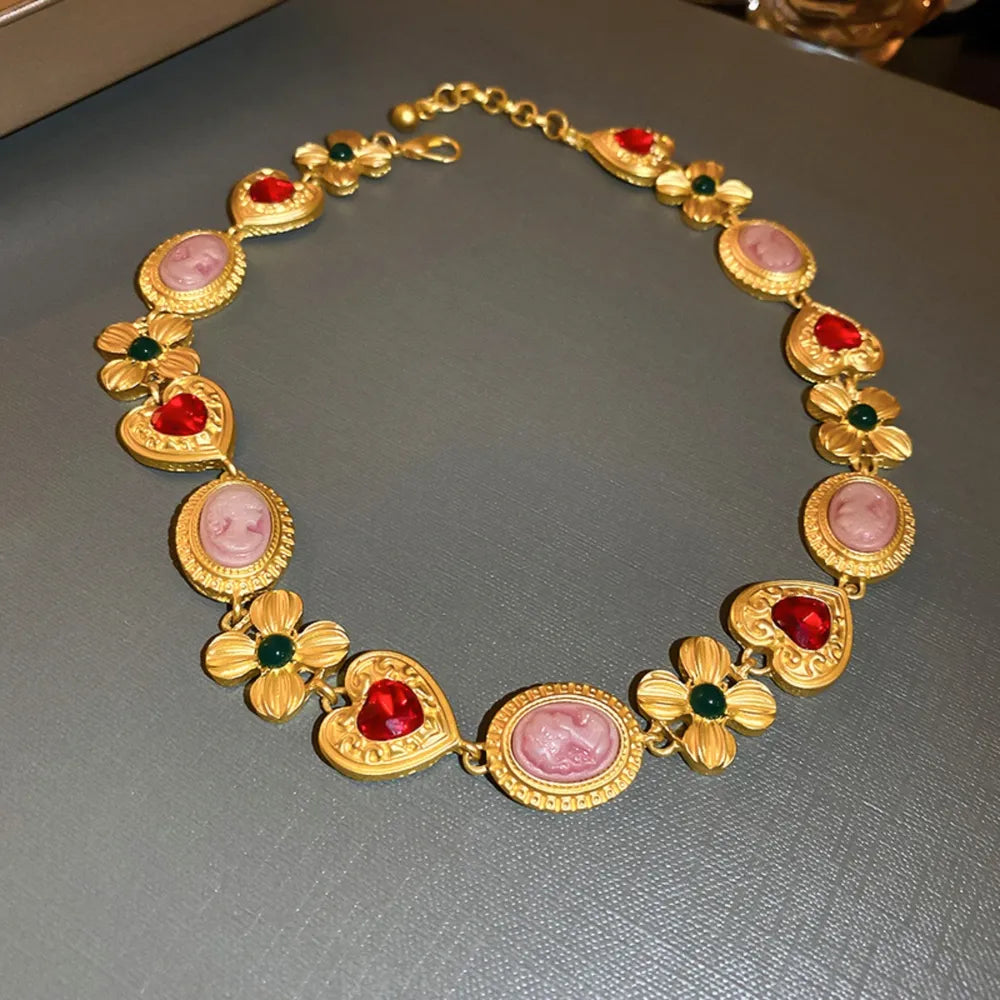 Gold statement necklace with cameo, heart, and floral charms with red and green accents.