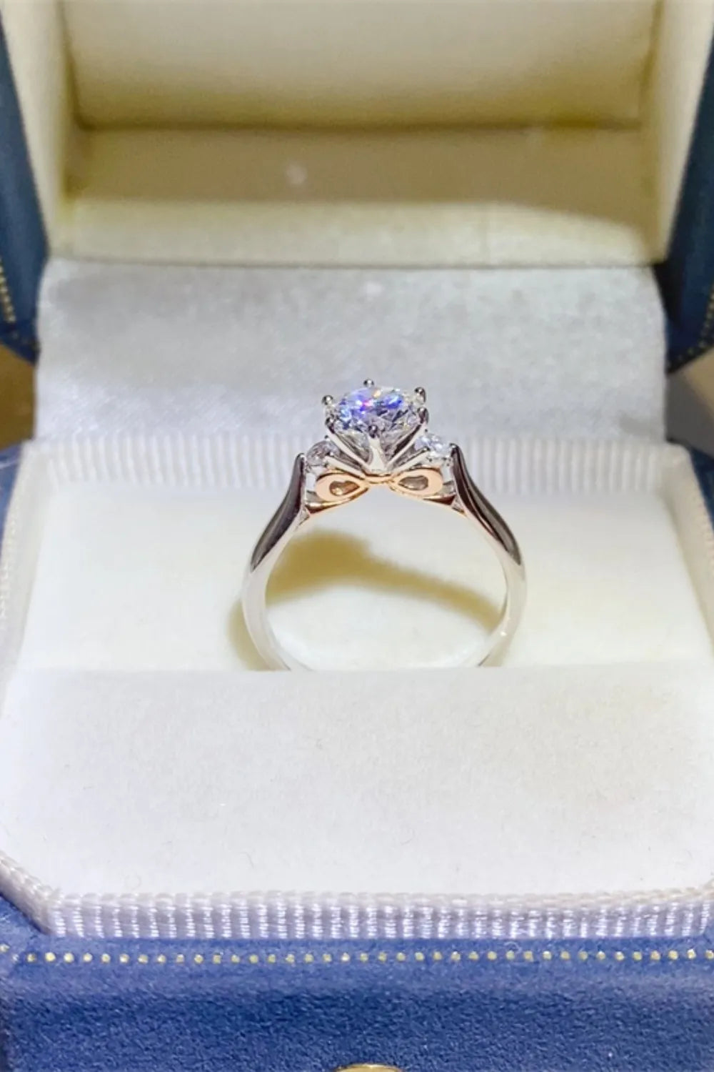 Silver moissanite trilogy ring with rose gold bow detail on band.
