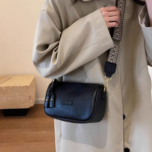 Black textured PU leather crossbody bag with tassel detail and patterned strap.
