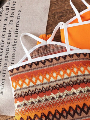 Baby halter dress with orange, brown, and cream zigzag knit pattern and white straps.