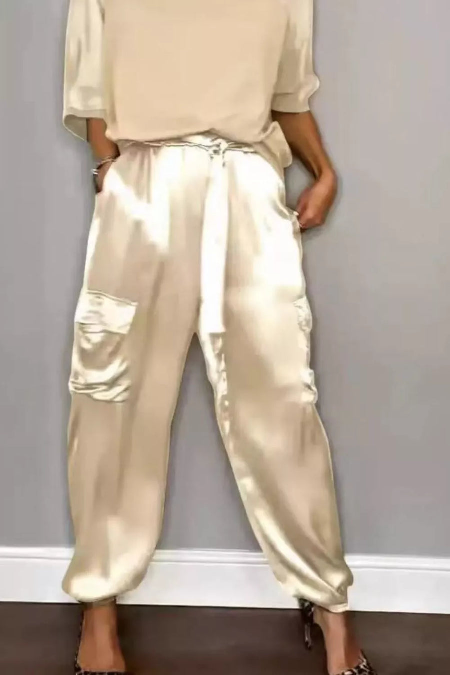 Beige satin two-piece ensemble with cargo pockets and a tie waist, styled with heels.