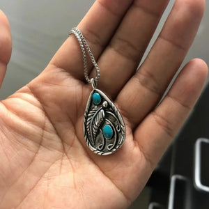 Silver pendant with turquoise stones and feather detail on a chain.