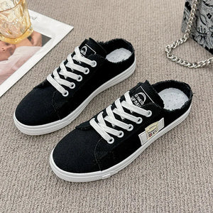 Black denim mule sneakers with raw edges and white laces.