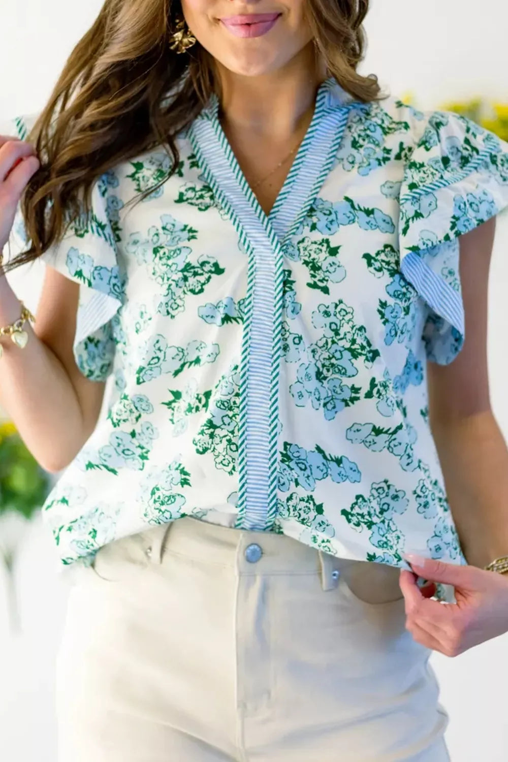Floral print polyester blouse with flutter sleeves, v-neck, and ruffled trim.