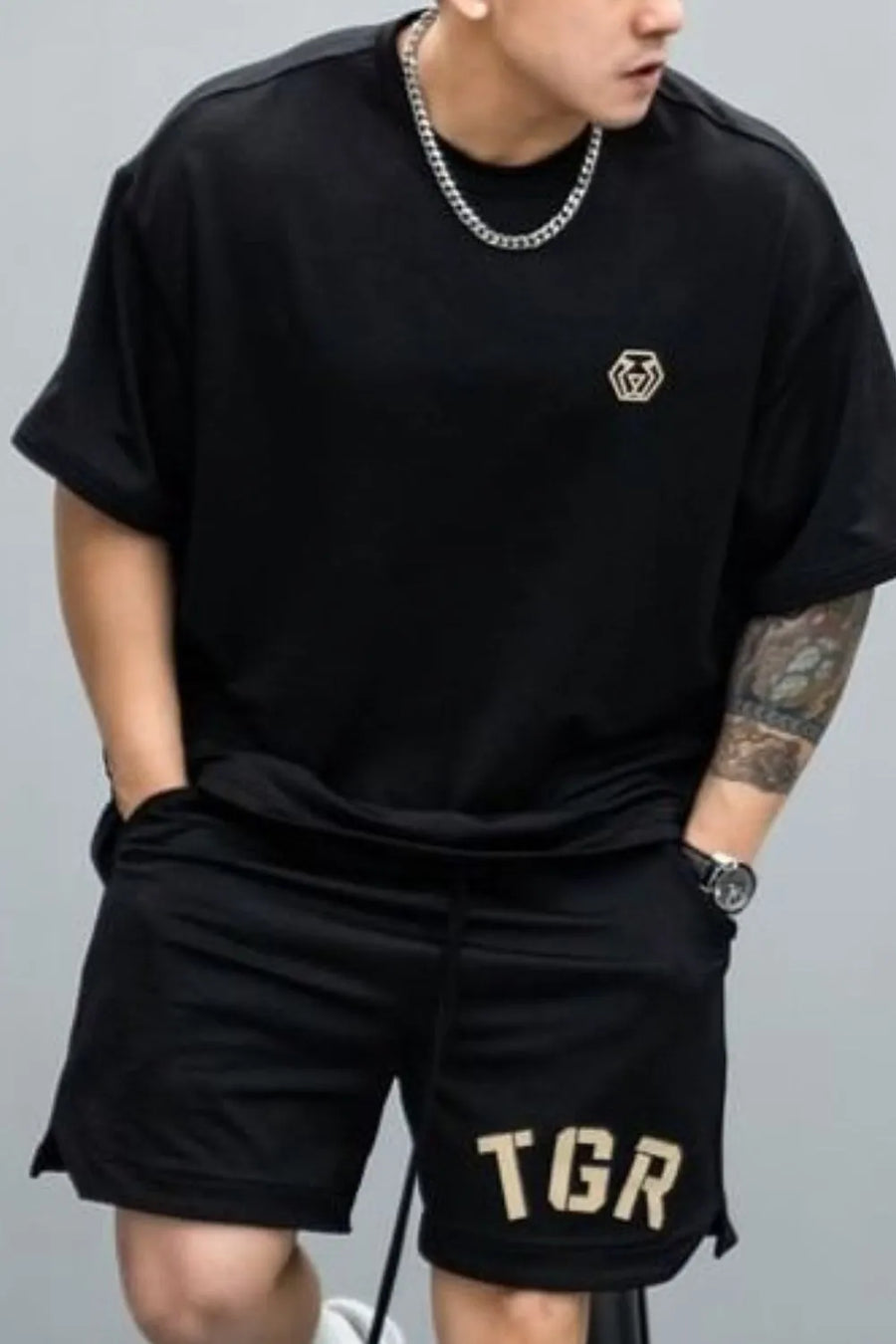 Black oversized tee with minimalist gold emblem on chest, short sleeves.