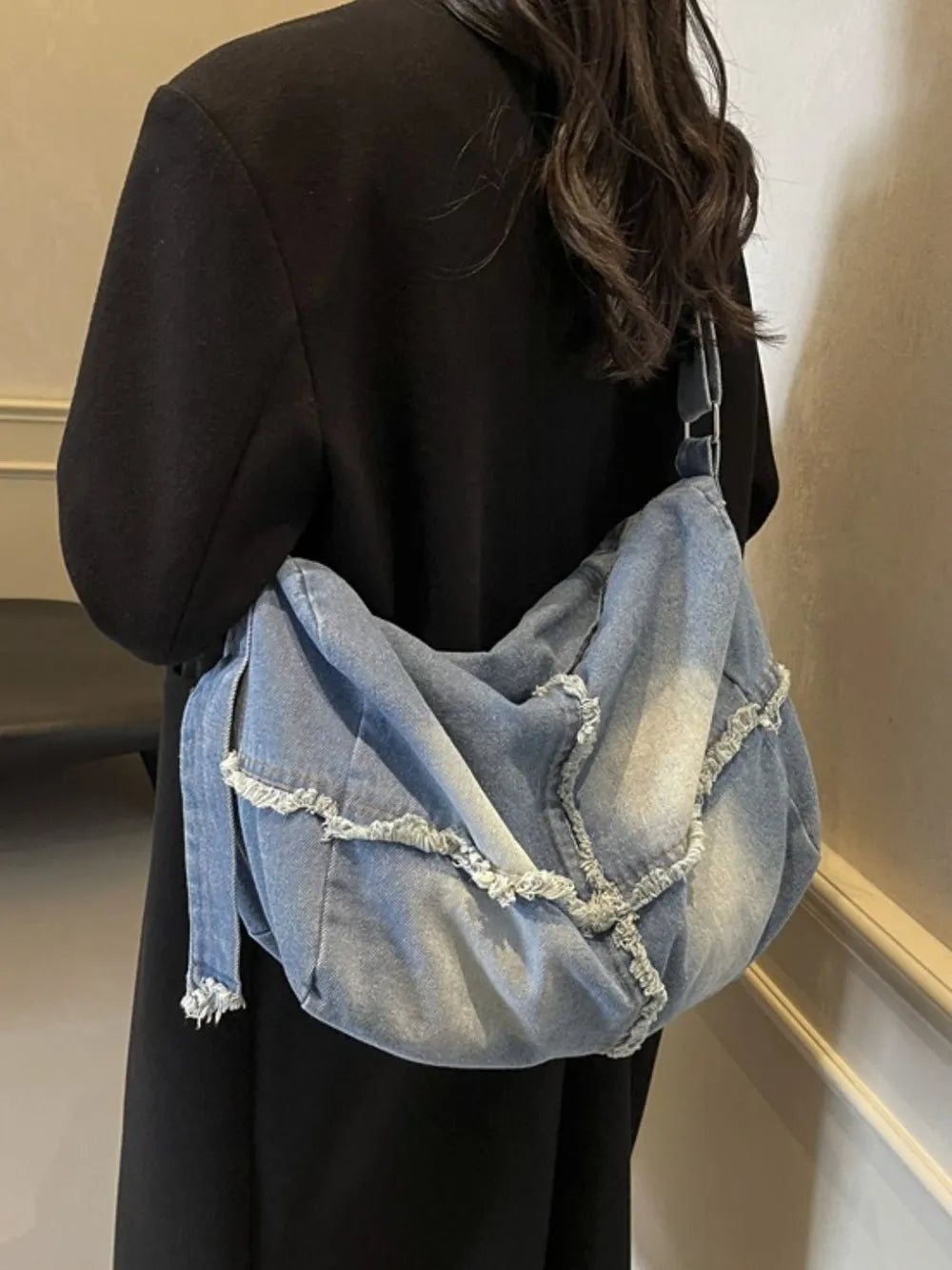 Frayed denim slouch crossbody bag in light blue with raw edges and a casual, relaxed style.