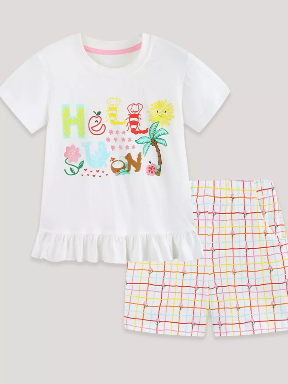 Girls' white cotton tee with ruffle hem and graphic print, paired with plaid shorts.