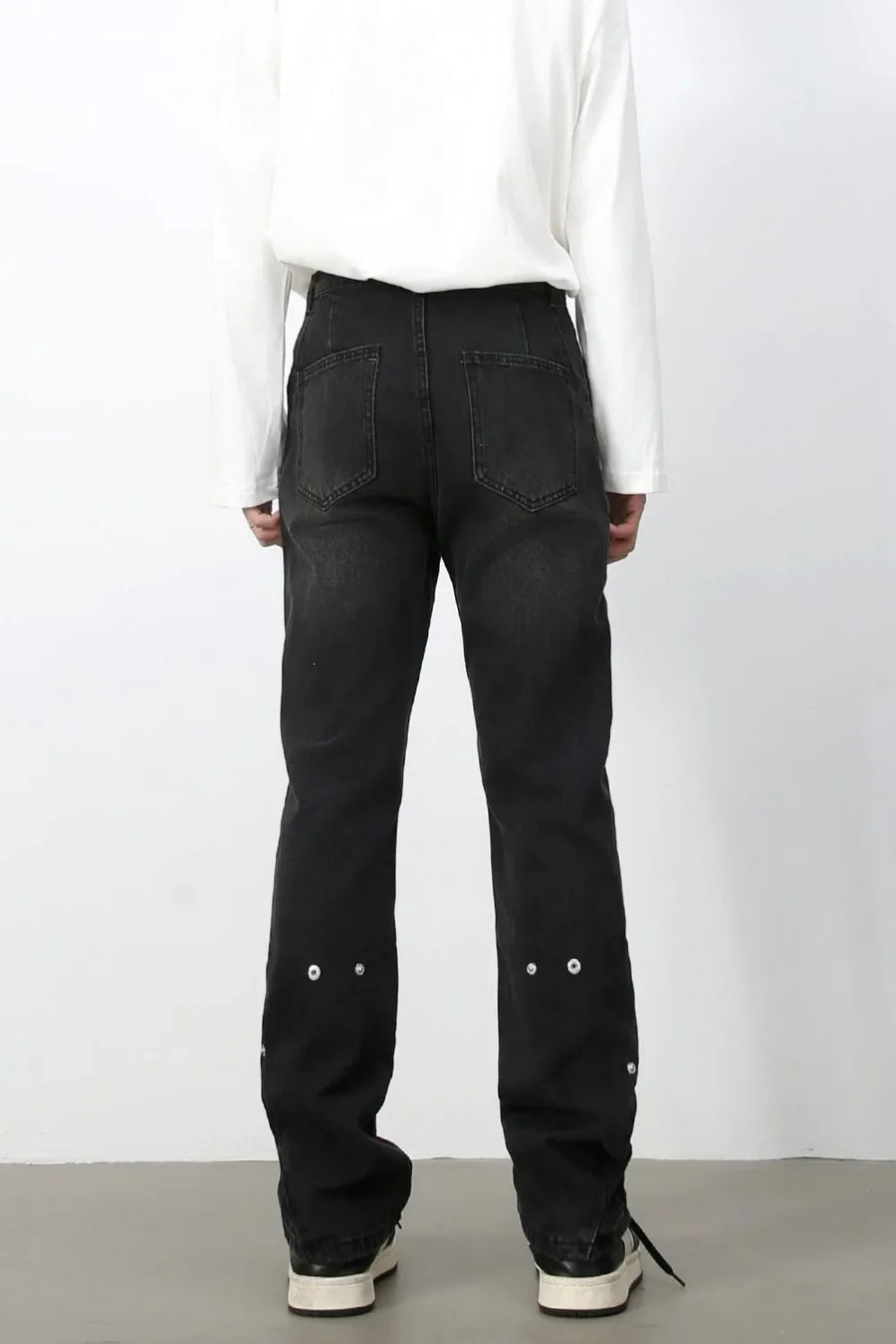 Dark wash denim trousers with asymmetric seams and decorative grommets on the lower legs.