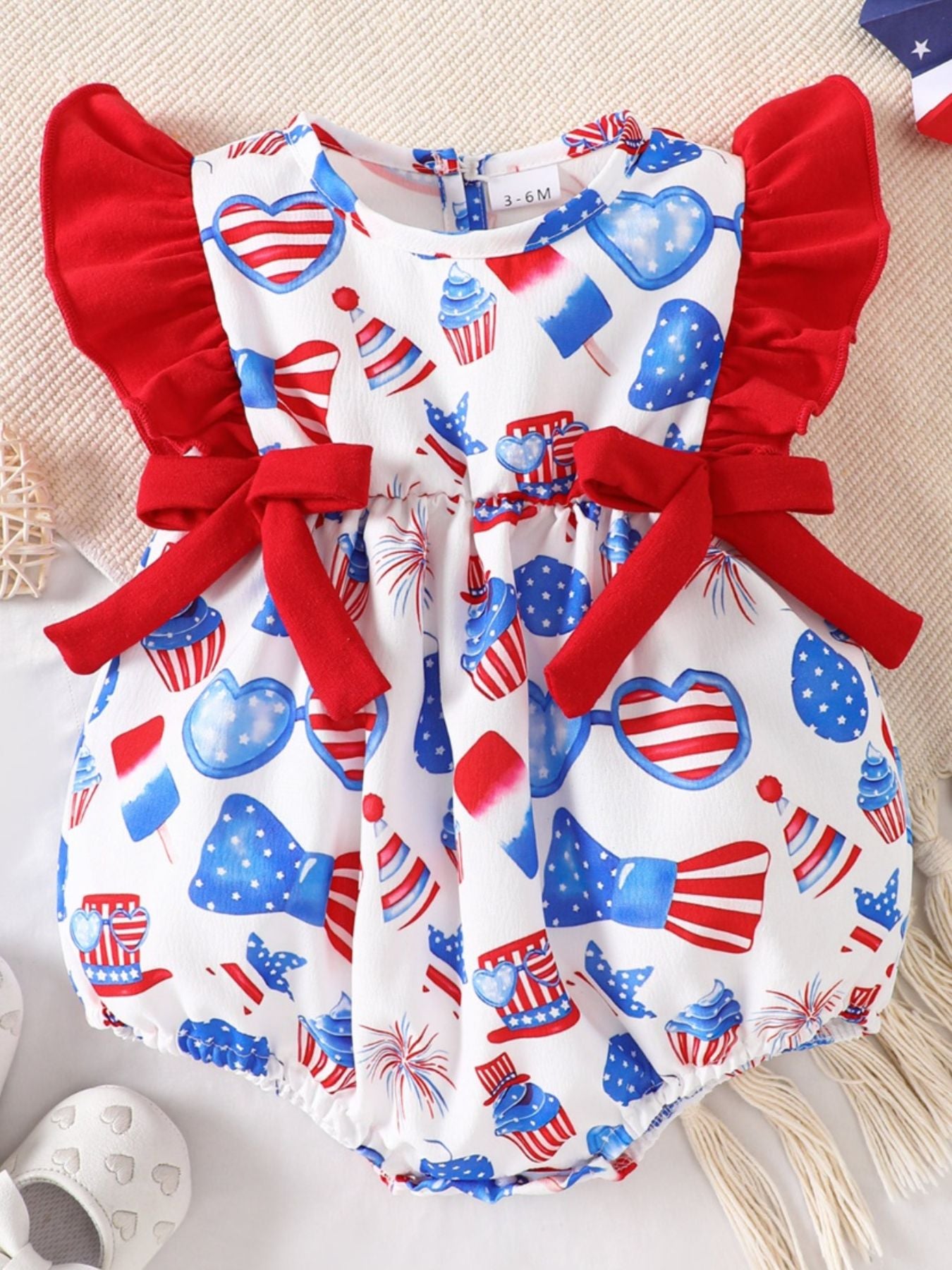 Baby patriotic print one-piece with ruffle sleeves and red bow accents.