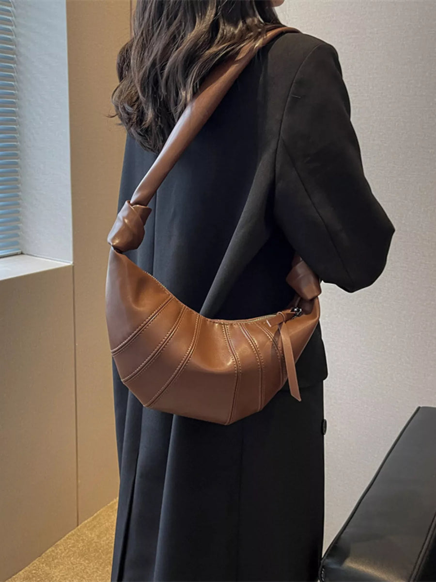 Brown crescent hobo crossbody bag with stitched panel details and knotted strap.