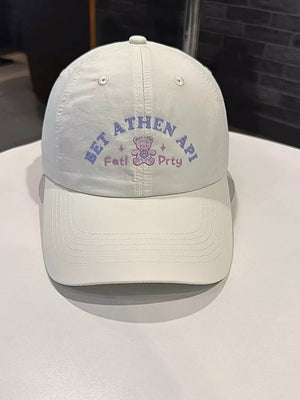 White baseball cap with purple embroidered text and a teddy bear graphic.