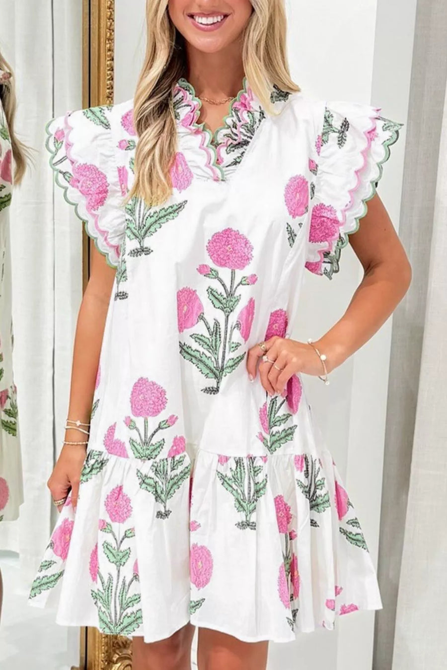 White mini dress with pink floral print, ruffled sleeves, and green scalloped trim.