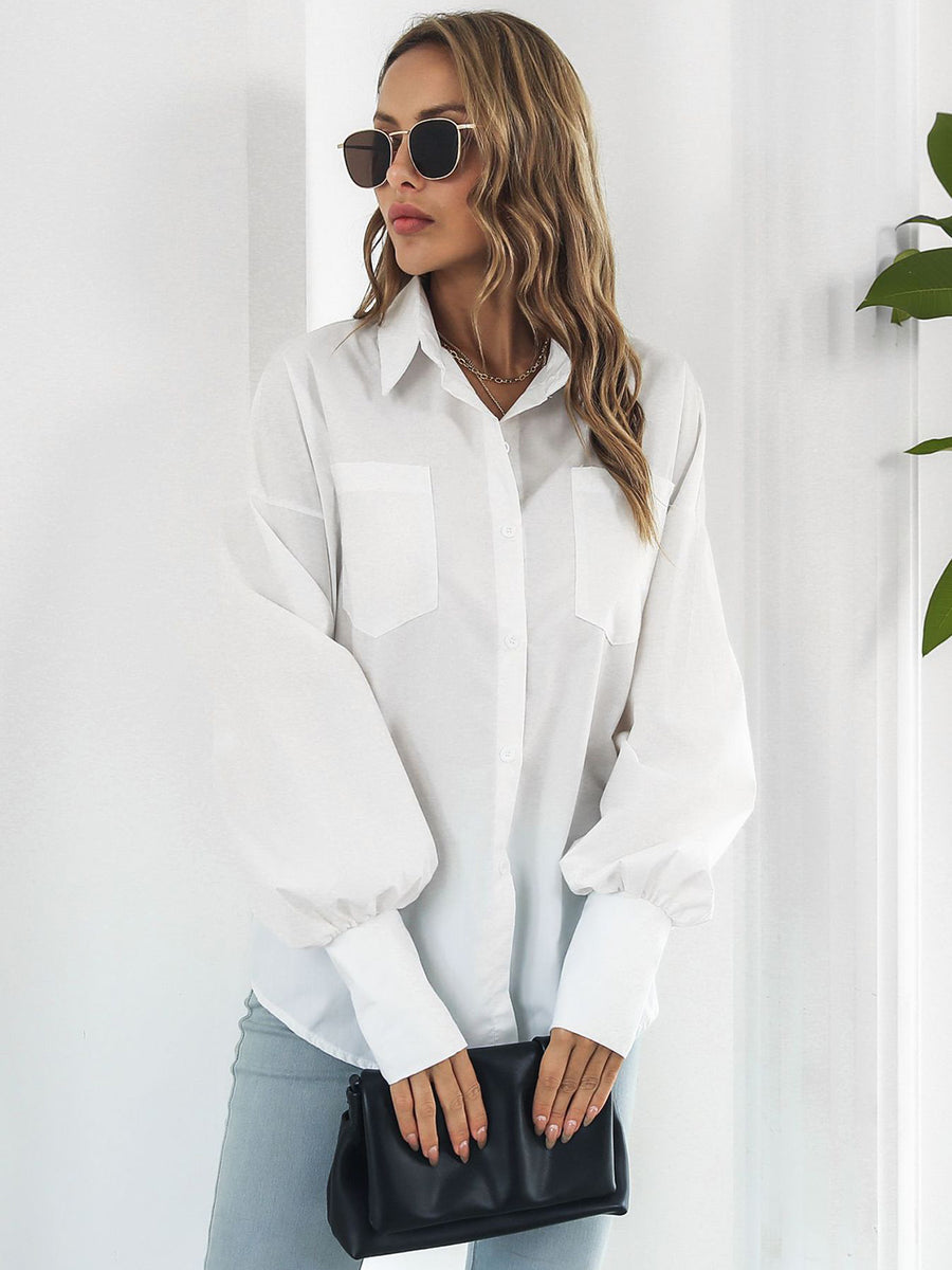 White oversized poplin blouse with blouson sleeves and button front, styled with light wash jeans and a black clutch.