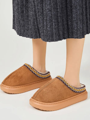 Caramel shearling house slippers with embroidered trim and faux fur lining.
