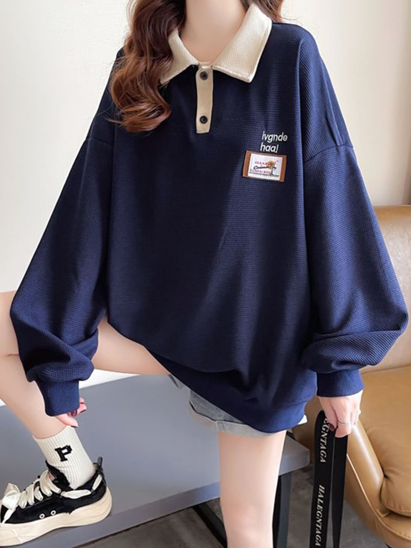 Navy waffle-knit polo sweatshirt with a contrast collar and button placket, featuring a graphic patch.