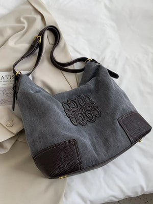 Medium canvas tote bag in gray with brown leather accents and embroidered logo detail.
